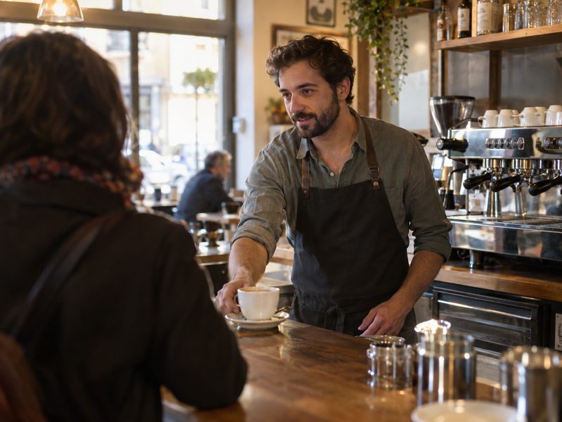 Camarero sirviendo un café detrás de la barra de un bar